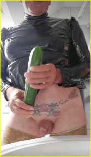 Cross-dressing anal whore Stacy holds a cucumber that he's about to shove in his arse